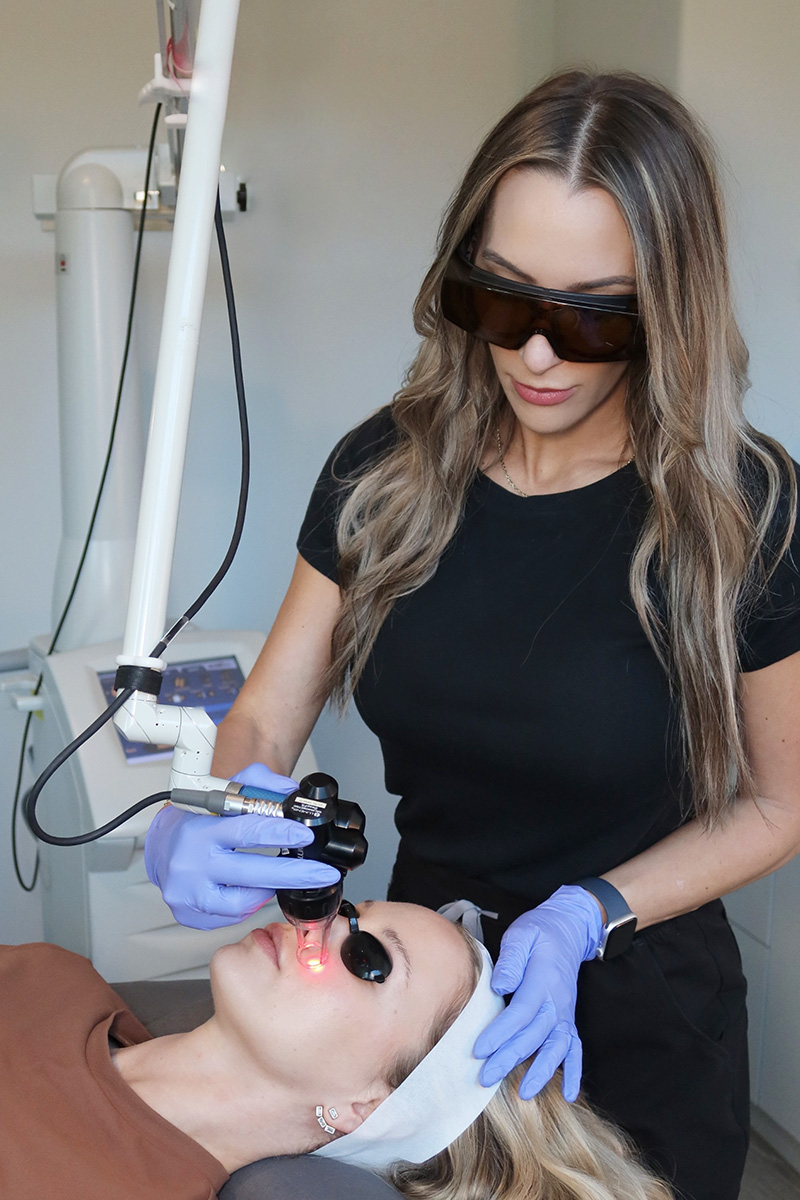 an Evolve Aesthetics team member performing a facial laser treatment an Evolve Aesthetics team member performing a facial laser treatment